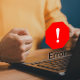 Una persona con el puño apretado en frente de un ordenador y una señal de error, mantenimiento preventivo y correctivo